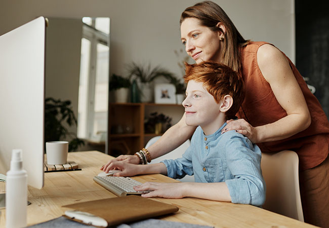 GIF selber machen: Junge sitzt am PC, Mutter steht helfend hinter ihm. Bild: Pexels/Julia M Cameron
